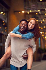 Fototapeta premium Portrait Of Young Couple Enjoying City Life Heading For Night Out With Man Giving Woman Piggyback
