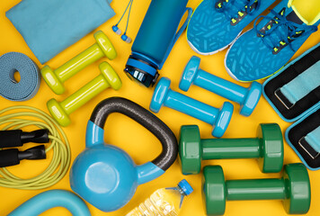 Dumbbells, trainers, jumping rope and other fitness equipment on yellow background, top view