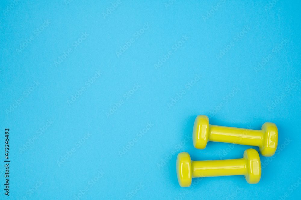 Wall mural Yellow dumbbells on blue background, top view with copy space