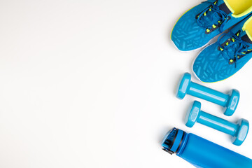Blue dumbbells, trainers and a water bottle on white background, top view with copy space