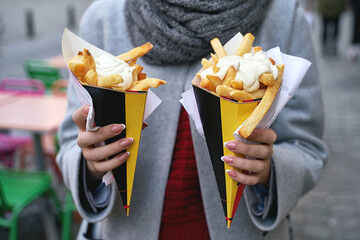 Belgian frites or french fries with mayonnaise in Brussels, Belgium. Female tourist holds two portions of fries in hands in the street. - obrazy, fototapety, plakaty