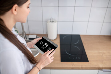 Housewife turning on the cooktop using a gadget