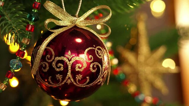 Close up of christmas ball on branch of Christmas tree on background of shining lights of golden garland. New Year