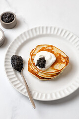 Black Caviar on pancakes with sour cream Holiday morning Appetizer on white plate and marble...