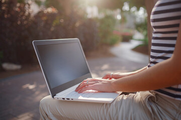 Female hands on laptop, woman types on keyboard sitting in park.