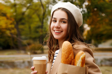 Portrait of pretty young french teenager girl in white beret holding baguettes and coffee or tea in...