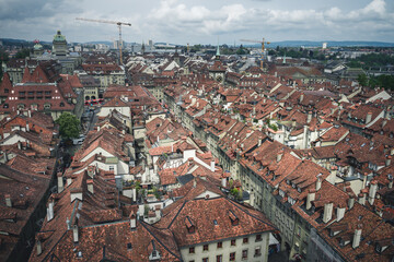 Fototapeta na wymiar A view of the cityscape of Bern, Switzerland with stone rooftops, streets below, and the farmer's market - a cloudy spring day with green trees and hills in the background