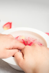 Hands in white bowl bathe nails with water and rose petals to soften the cuticle and dry skin