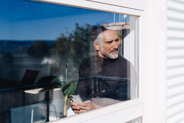 Aged male using mobile phone behind glass window