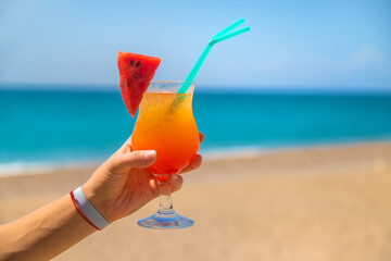 A woman holds a cocktail in her hand against the background of the sea. Selective focus.