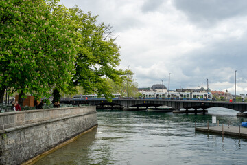 The Limmat River flows next to the cityscape of Zurich, Switzerland on a cloudy spring afternoon - trees and buildings line the river