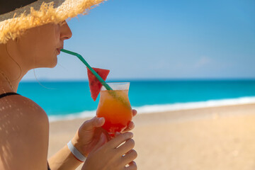 A woman holds a cocktail in her hand against the background of the sea. Selective focus.