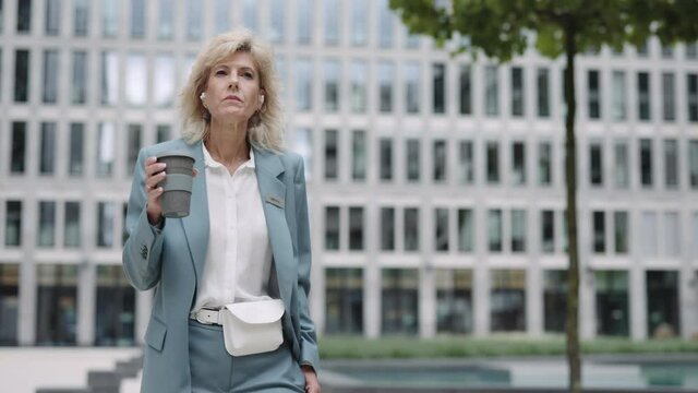 Business woman in earphones drinking coffee and walking