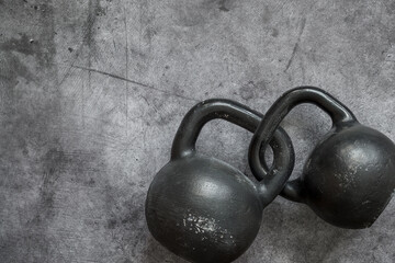 Naklejka na ściany i meble Two kettlebells with intertwined handles lie on a cement gray background.