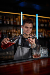 Bartender in apron adds ingredient to glass