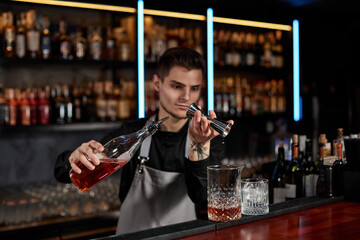 Bartender in apron adds ingredient to glass