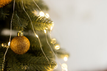 Close up of gold ball toy and garlands on green-yellow Christmas tree