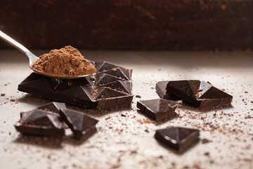 Dark chocolate is broken into pieces on the table. A spoonful of cocoa powder. Copyspace