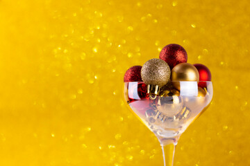 Cocktail glass filled with red and yellow Christmas tree balls on yellow bokeh abstract background. Christmas or new year creative background.