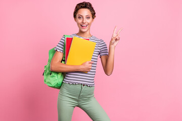 Photo of optimistic young school lady hold books show v-sign wear bag white t-shirt jeans isolated...
