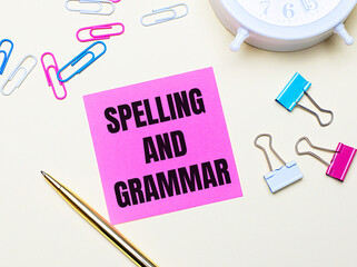 On a light background, a white alarm clock, pink, blue and white paper clips, a golden pen and a pink sticker with the text SPELLING AND GRAMMAR