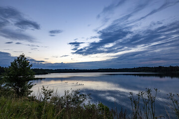 a beautiful blue lake with green tree in the foreground under a dramatic blue dusk sky. High quality photo