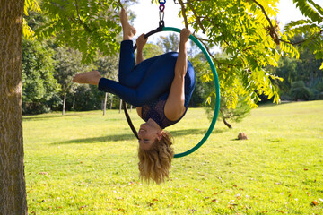 Blonde woman and young gymnast acrobat athlete performing aerial exercise on air ring outdoors in park. Lithe woman in blue costume performs poses of circus performers dancing with hips