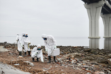 Fototapeta na wymiar Wide angle view at group of workers wearing hazmat suits gathering samples of soil by water outdoors, toxic waste concept, copy space