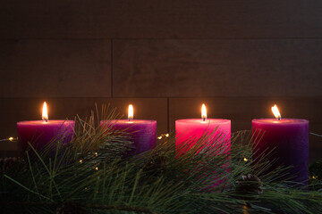 Four candles lit in advent wreath for fourth week of advent with pillar candles on dark wood