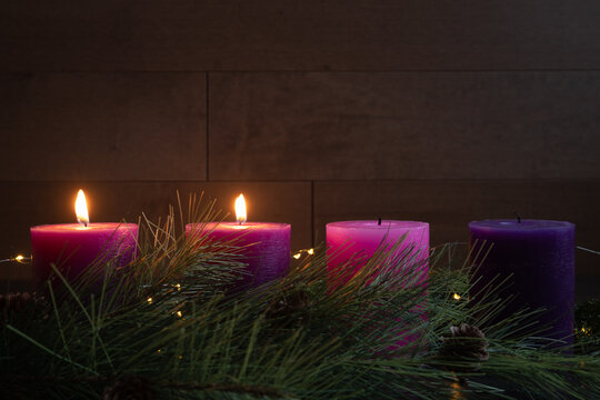 Two candles lit in advent wreath for second week of advent with pillar candles on dark wood