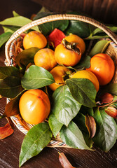 persimmon with leaves on the branches in a basket on the wooden background