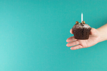 Birthday holiday. Chocolate muffin with candles in a female hand. Homemade dessert on a blue...