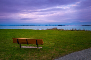 Dramatic purple cloudscape and an empty bench in the park. Twilight seascape over the green at Nut...