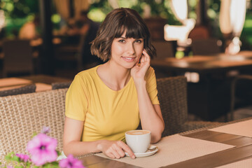 Photo of dreamy charming young lady dressed yellow t-shirt sitting cafeteria drinking beverage smiling outdoors urban park