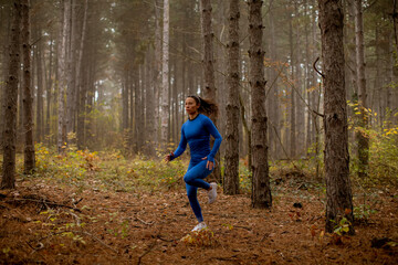 Fototapeta premium Young woman running on the forest trail at autumn