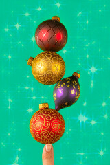 Finger balancing christmas ornaments on a teal stary background