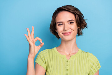 Photo of shiny pretty young woman dressed green t-shirt smiling showing okey sign isolated blue color background