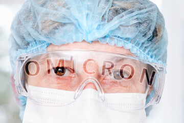 Close-up tired eyes of doctor through goggles and word omicron in reflection, new coronavirus covid...