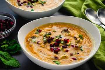 Bowls of Moroccan Roasted Pumpkin Soup: Roasted pumpkin soup garnished with mint leaves, pomegranate seeds, and chopped pistachios