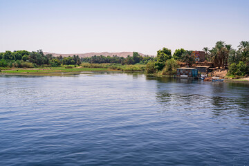 View across the Nile River to nature among the palm trees and the desert, with a small rural port in the interior. Photograph taken in Aswan, Egypt. 