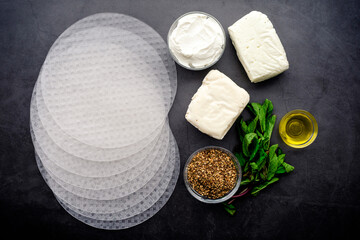 Ingredients for a Middle Eastern Fusion Cuisine Appetizer: Spring roll wrappers, halloumi cheese, and other ingredients on a dark background