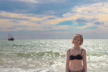 Beautiful woman in a swimsuit on the seashore with a sailing ship. Travel and tourism