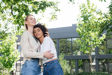 smiling young woman hugging curly girlfriend outside