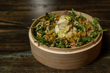 Burrata salad with arugula leaves with pesto sauce and pieces of fried bread with parsley and garlic accompanied by pesto sauce and served in a bamboo bowl