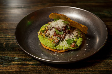 Corn cake or taco stuffed with avocado and different organic vegetables with a lime and cinnamon dressing and cheese sprinkled on top