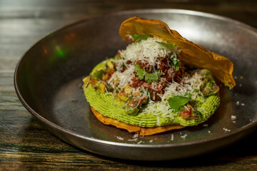 Corn cake or taco stuffed with avocado and different organic vegetables with a lime and cinnamon dressing and cheese sprinkled on top