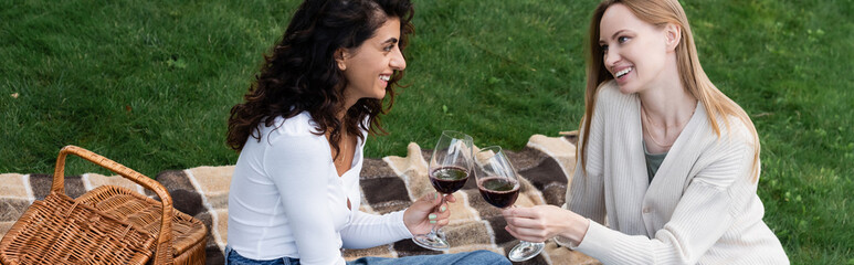 happy lesbian couple clinking glasses of red wine during picnic, banner