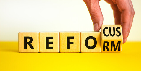 Refocus and reform symbol. Businessman turns a wooden cube and changes the word refocus to reform. Beautiful yellow table, white background. Business refocus and reform concept. Copy space.