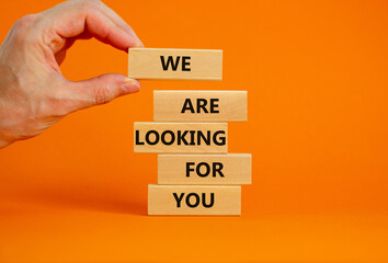 We are looking for you symbol. Wooden blocks with words We are looking for you. Businessman hand. Beautiful orange background, copy space. Business, we are looking for you concept.