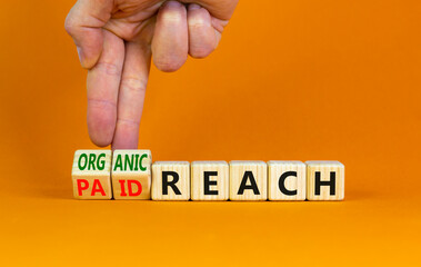 Organic or paid reach symbol. Businessman turns wooden cubes and changes words paid reach to organic reach. Beautiful orange table orange background copy space. Business organic or paid reach concept.